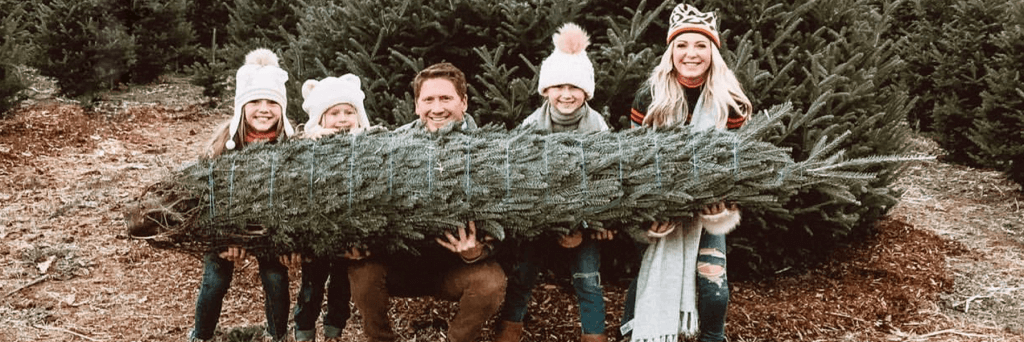 A family of 5 holding their real Christmas tree at a tree farm