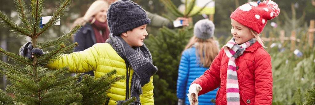 Two children smiling at each other next to a Christmas tree